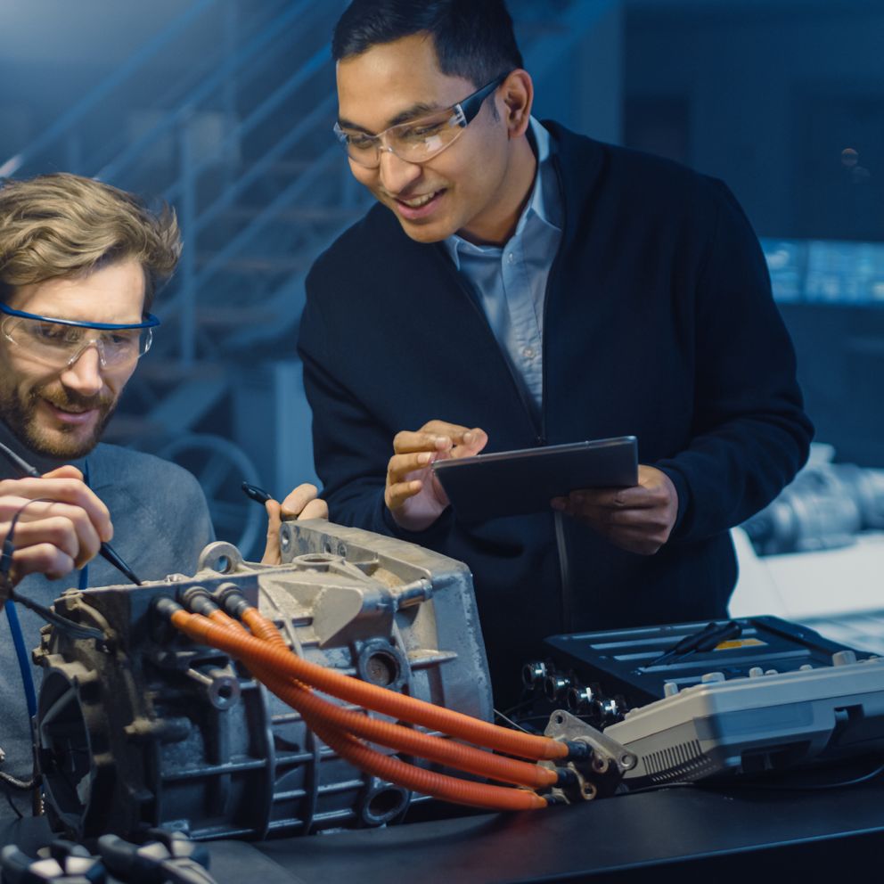 Zwei lächelnde Männer arbeiten an der Technik eines Elekto-Fahrzeuges